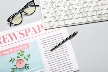 Newspaper with pen, computer keyboard and eyeglasses on light background, closeup