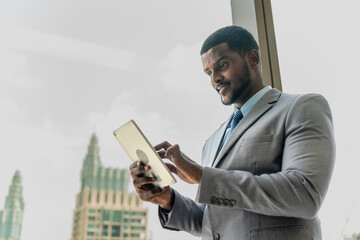 Handsome black businessman with a digital tablet over a glass window overlooking the city skyline