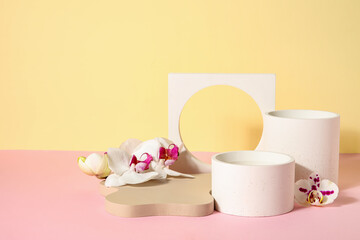 Decorative plaster podiums and beautiful orchid flowers on pink table against beige background