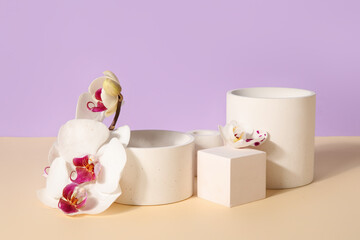 Fototapeta na wymiar Decorative plaster podiums and beautiful orchid flowers on beige table against lilac background