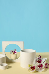 Fototapeta na wymiar Decorative plaster podiums and beautiful orchid flowers on beige table against blue background