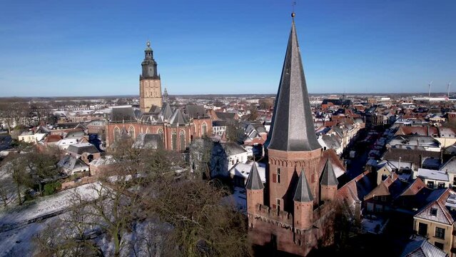 Cinematic aerial pan movement showing historic Dutch tower town Zutphen Drogenapstoren city entrance in the foreground and Walburgiskerk cathedral behind in snow winter wonderland on sunny day