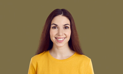 Studio headshot of a beautiful brunette woman with a happy face expression. Portrait of a cheerful young girl in a yellow T shirt smiling and looking at the camera isolated on a brown background