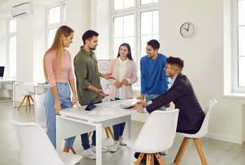 Smiling diverse young people brainstorm discuss business ideas or projects in office. Happy multiracial colleagues or employees coworking engaged in team meeting. Teamwork concept.