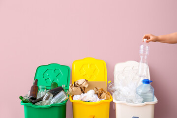 Woman throwing garbage into trash bin near pink wall. Recycling concept - obrazy, fototapety, plakaty