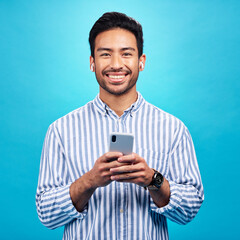 Happy, portrait and a man with a phone for communication isolated on a blue background in a studio....