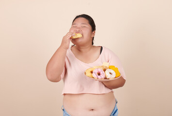 Happy fat woman eating donuts on plate isolated on color background. Food addiction, diet breakdown, eating disorders, depression, laziness problem eating, compulsive overeating concept.