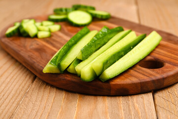 Board with fresh cut cucumber on wooden background, closeup