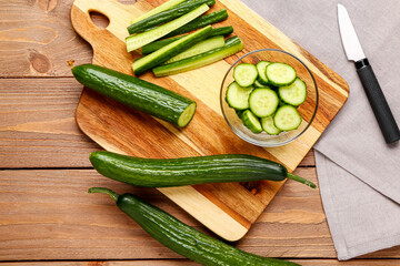Bowl with cut and whole cucumbers on wooden wooden background