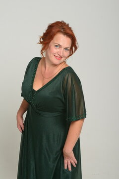 Image of pretty redhead young lady in green dress standing with arms crossed over grey wall background. Looking camera woman redhead green dress
