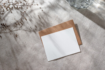 Blank paper card with mock up copy space and envelope on beige linen background with aesthetic sunlight shadows, invitation or greeting card template