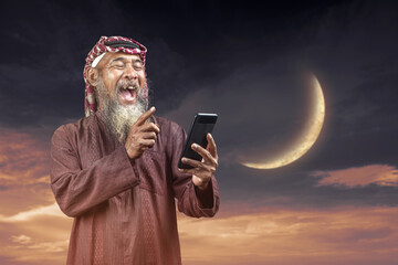 Muslim man with a beard wearing keffiyeh with agal using a mobile phone