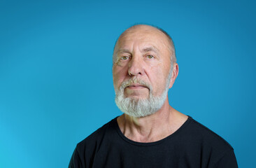 Portrait of an elderly man with a gray beard in casual clothes. Black T-shirt, blue background