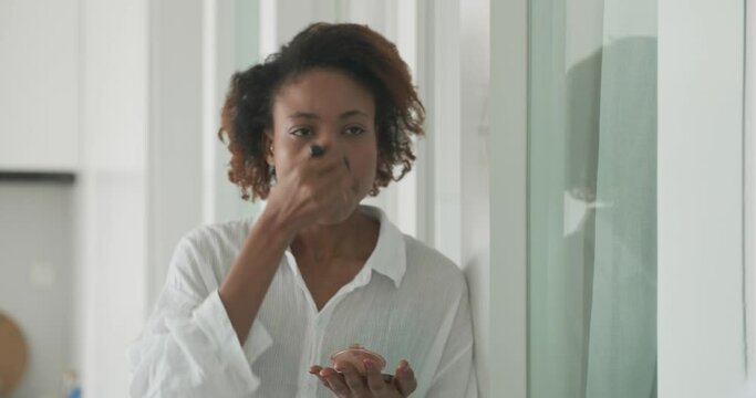 young African woman makeup with powder brush on the mirror, young woman puting on makeup carefully