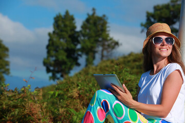 Happy young woman using tablet pc on the beach with mountains in the background