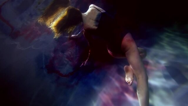 art underwater shooting, graceful lady swimming and playing with red and blue dyes in depth