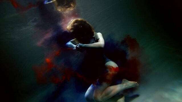 graceful woman floating in death and coloring water in blue and red, amazing fantasy underwater