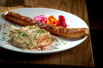 Bavarian meat sausage with a garnish of stewed mushrooms in sour cream, onions in a plate on a wooden background