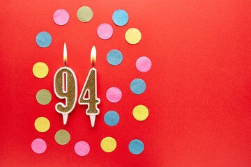 Number 94 on a red background with colored confetti. Happy birthday candles. The concept of...