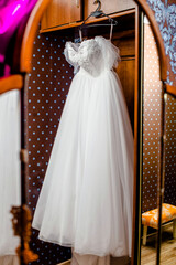 The bride's white dress hangs on a hanger

