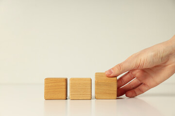 Three wooden cubes on white table and female hand, close up