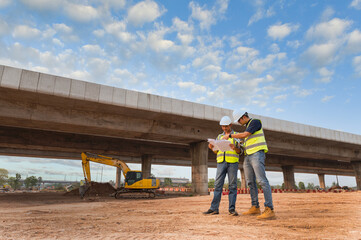 Asian architect and mature supervisors meeting at construction site Multiethnic workers and engineers discussing plans Two construction workers working together while visiting expressway construction
