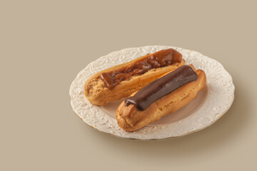 Two eclairs with different types of fudge on a white vintage plate on a gray table