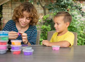 Naklejka premium boy of preschool age sits at table with older sister or nanny, they are molded from multi-colored mass for modeling. Spending time together is interesting and creative, games for children