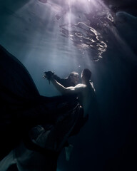 Fototapeta na wymiar love story girl in a beautiful long dress freediver dancing underwater with a partner in the pool