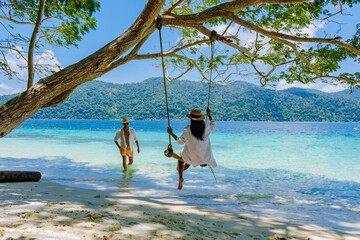 A couple of men and women are on the beach with a rope swing