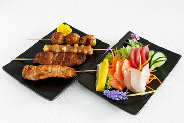Assortiment de sushi et brochettes yakitori une assiette noir et fond blanc. Cuisine japonaise.