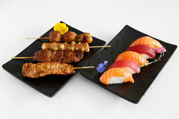 Assortiment de sushi et brochettes yakitori une assiette noir et fond blanc. Cuisine japonaise.