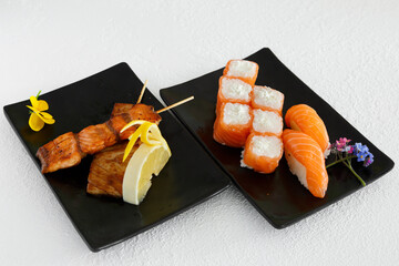 Assortiment de sushi et brochettes yakitori une assiette noir et fond blanc. Cuisine japonaise.