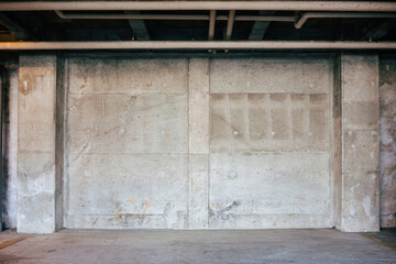 View of an empty parking space in an underground car park. Frontal view of a gray concrete wall and gray floor.