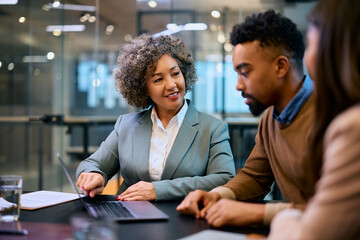 Happy bank manager using laptop while consulting young couple in office.