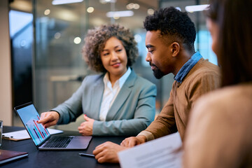 Smiling black man and financial consultant analyzing his investments on laptop in office.