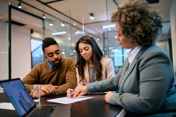 Young black couple signing contract with insurance agent in office.