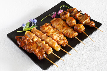 Assortiment de brochettes yakitori: brochette de poulet, brochette de boeuf fromage, brochette de saumon sur une assiette noir et fond blanc. Cuisine japonaise.
