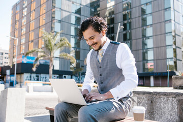 young latin businessman using laptop and phone working on computer in bench outdoors in Mexico city, Latin America hispanic people