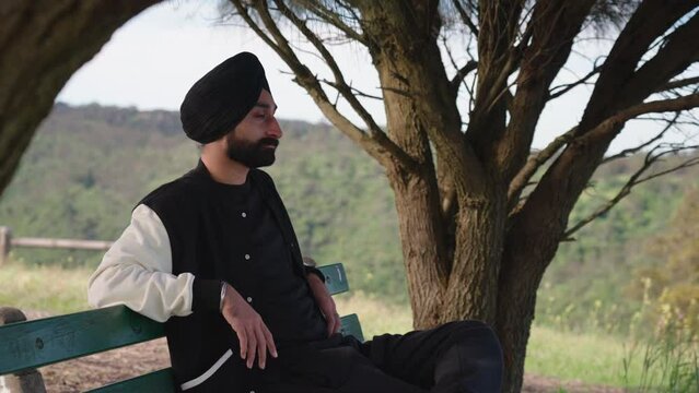 Handsome Punjabi Sikh Man Sitting On A Bench With Nature Background. Medium Shot