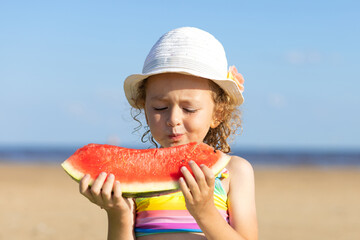 cute little girl eats ripe juicy red watermelon on the beach, coast, seashore. the concept of summer kid holidays, seasonal fruits and berries. portrait