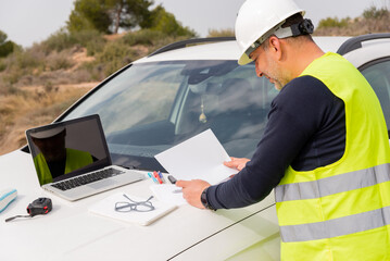 industrial engineer at construction site consulting blueprint or document next to a car at the construction site
