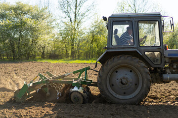 The tractor drives across the field and cultivates the land. Agricultural vehicle works in countryside. Sowing is the process of planting seeds in the ground as part of the early spring time