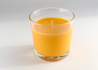 Orange scented candle in glass holder on the table. Paraffin candle in a clear glass made at home. One orange-scented candle in close-up.