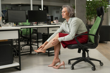 Caucasian woman massaging her tired legs while sitting in the office. 