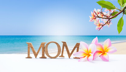 Fototapeta na wymiar Mother's day card background idea, tropical style, mom wooden font with plumeria flower over summer beach background