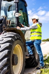 Engineer in safety helmet and reflective vest working on a tractor or backhoe at a construction site on a sunny day vertical 