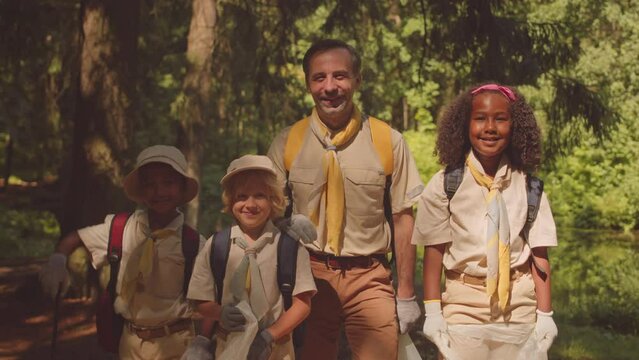 Medium portrait of cheerful multiethnic scout troop and their leader posing for camera after cleaning forest from rubbish together on sunny day