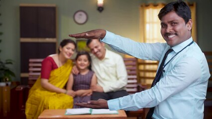 Happy indian banker showing hands like holding family using hand gesture by looking camera at home - concept of insurance protection, banking service and banking security
