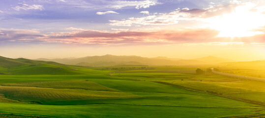 countryside sunset in green hills of spring fields with old castle farm and mountains on background of evening landscape